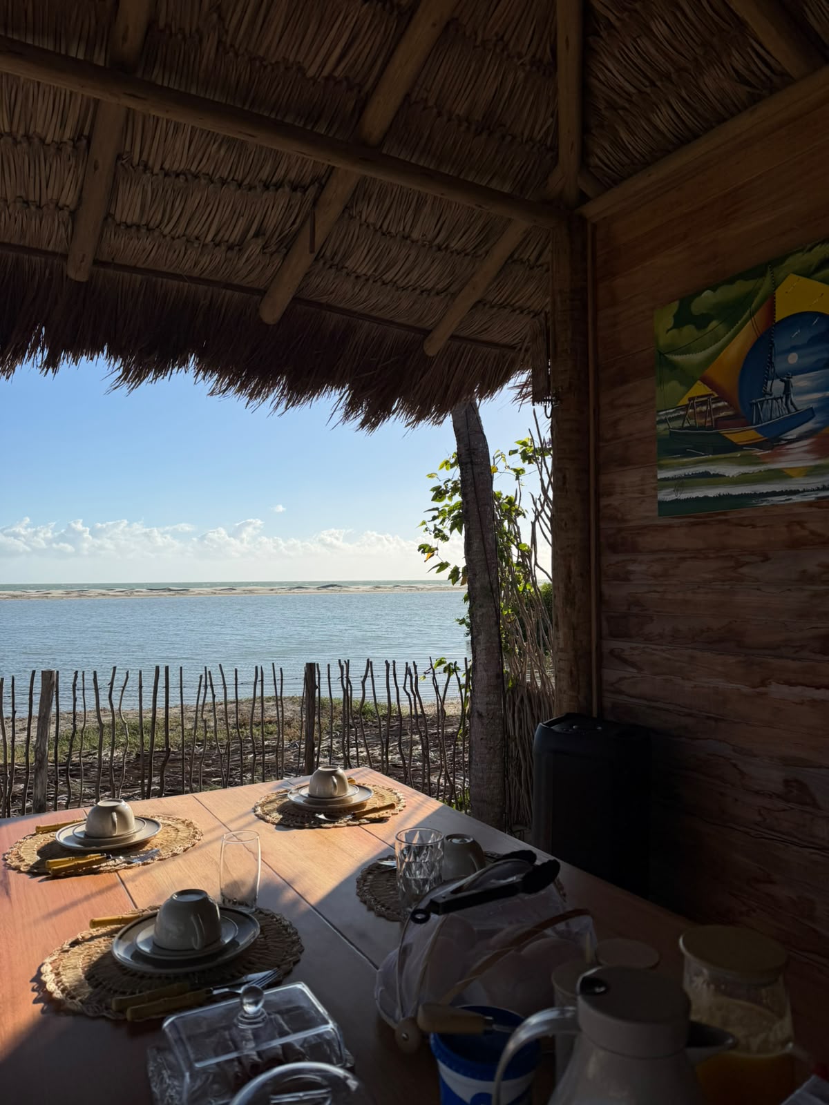 Mesa na varanda de palha com vista para o mar e uma turbina eólica no horizonte
