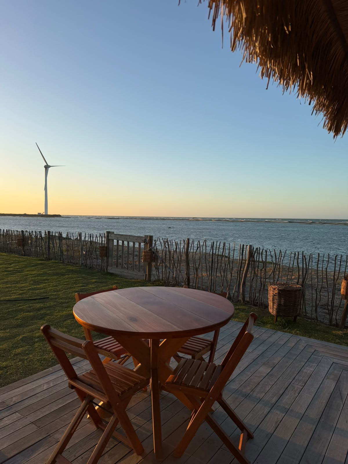 Mesa de café da manhã posta sob telhado de palha com vista para a lagoa